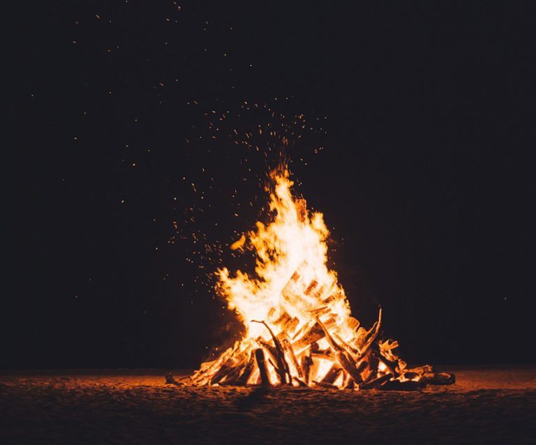 In front of a black background, a bonfire burns and spitting sparks into the air.