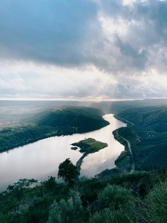 A panoramic view over a wide river flowing through a valley with a small island in the middle of it.