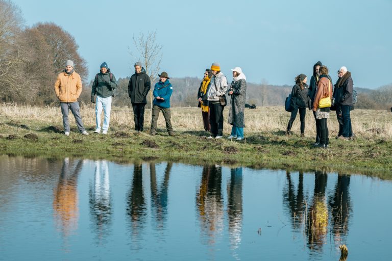 A group of young people standing around a pond in the sun.